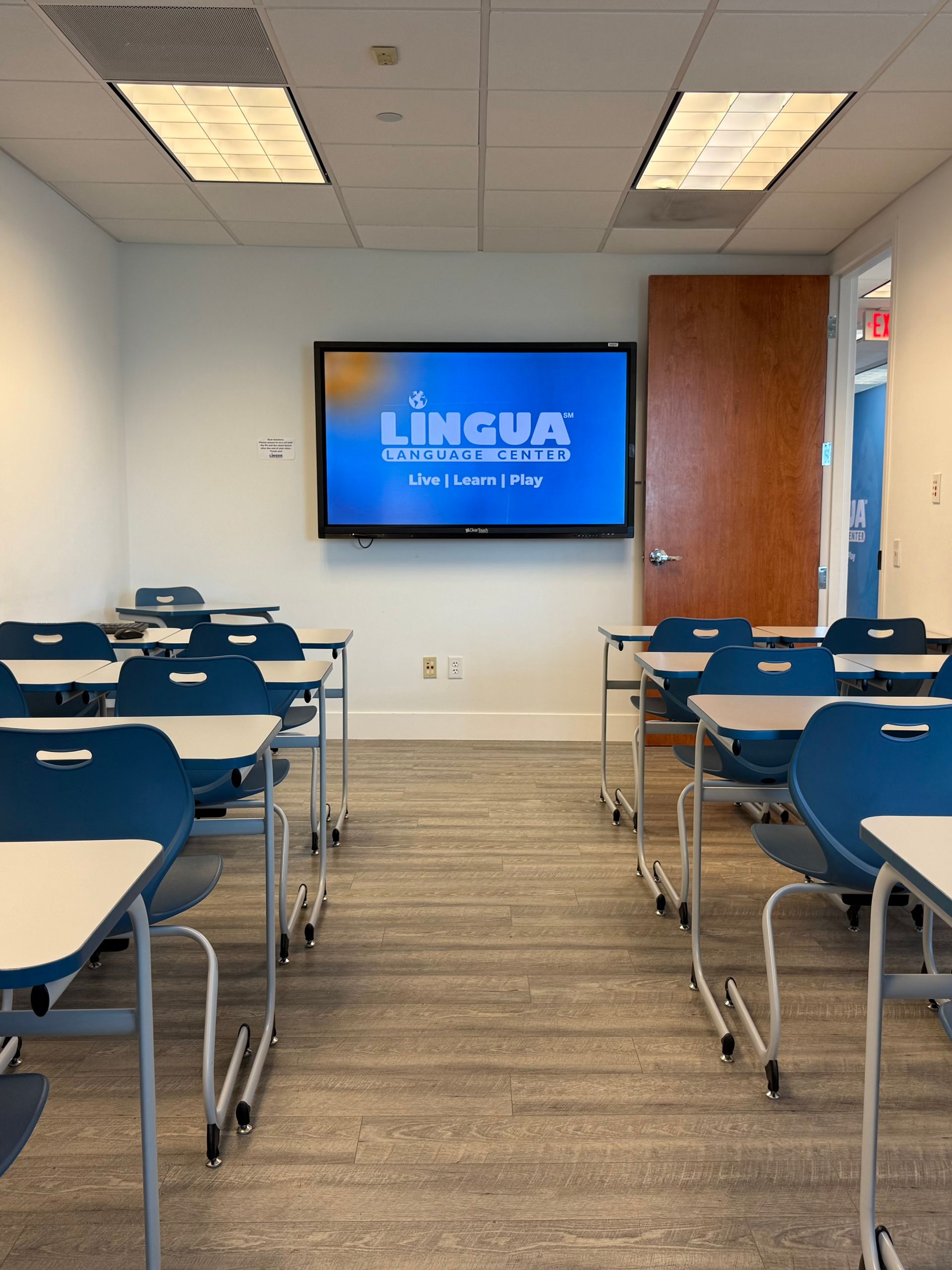 Empty classroom with blue desks and a wall-mounted TV displaying a presentation