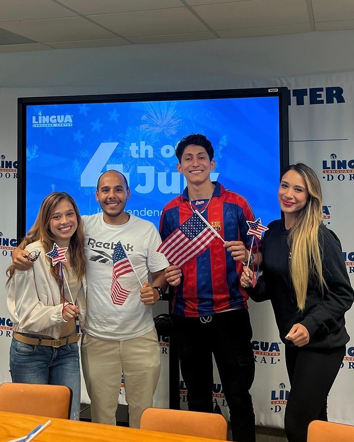 Four people posing indoors with small American flags in front of a blue event screen.