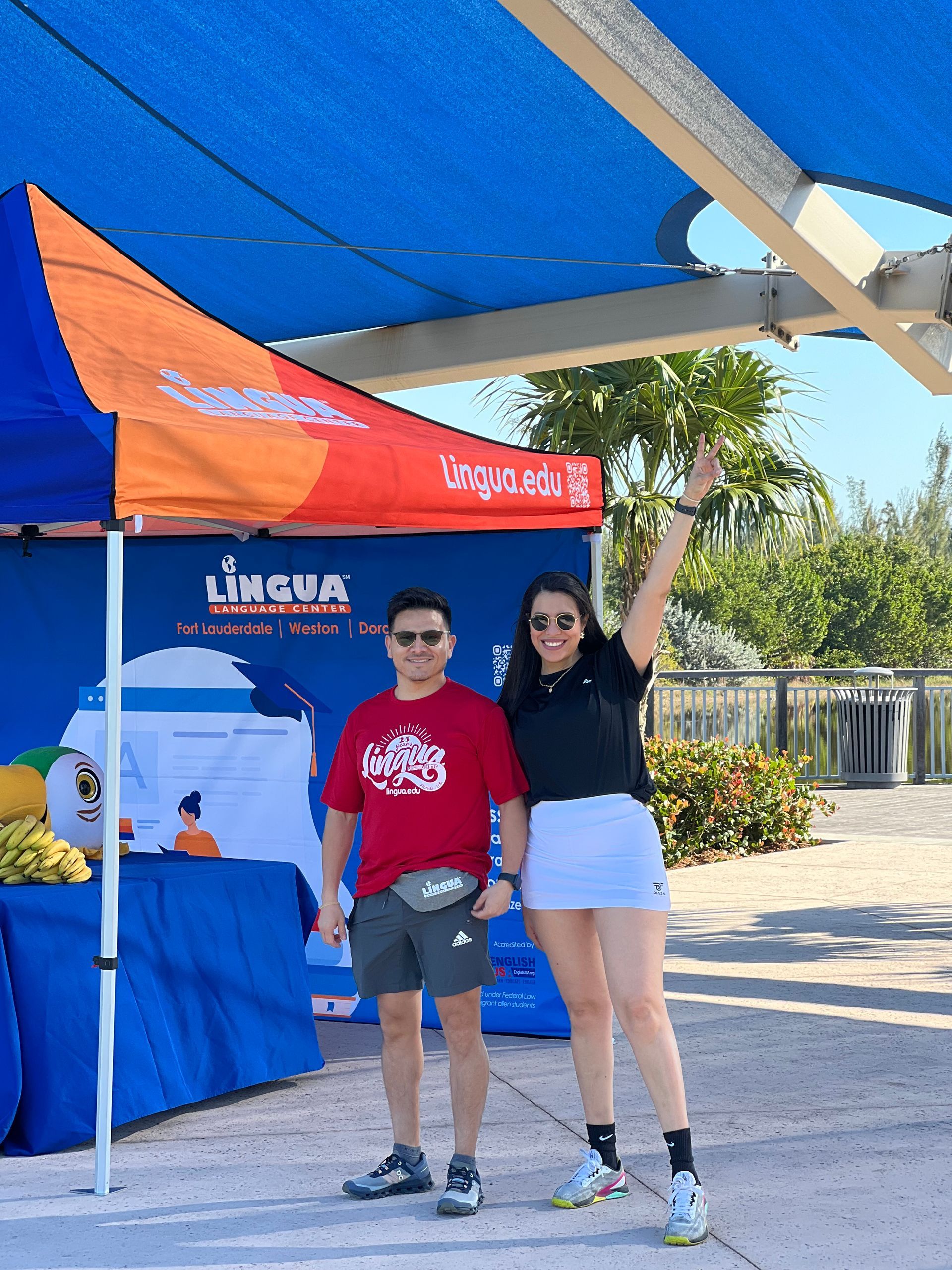 Two people posing under a blue-and-orange tent at an outdoor event booth.