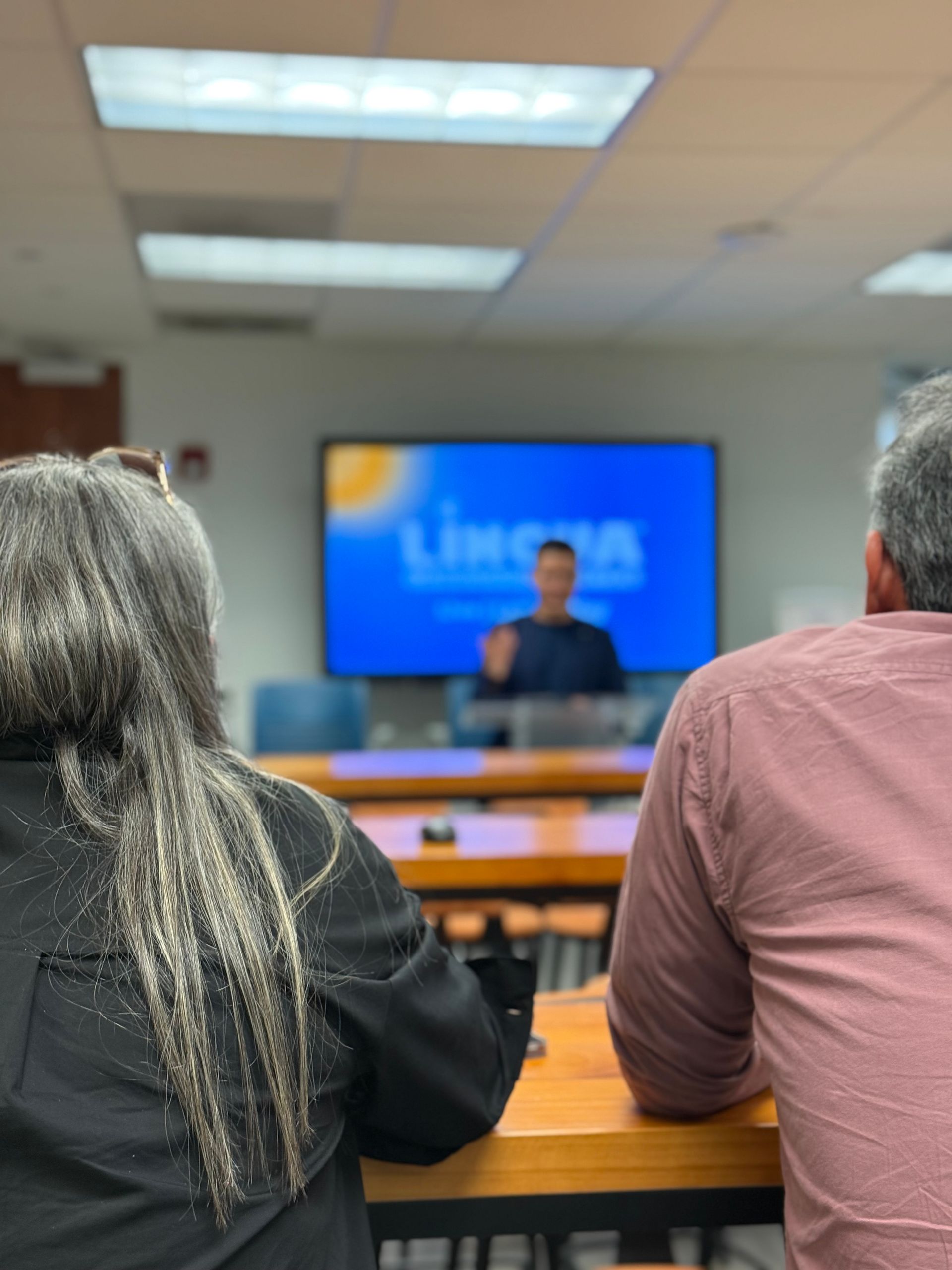 Audience seated in a classroom watching a speaker at a front screen during a presentation