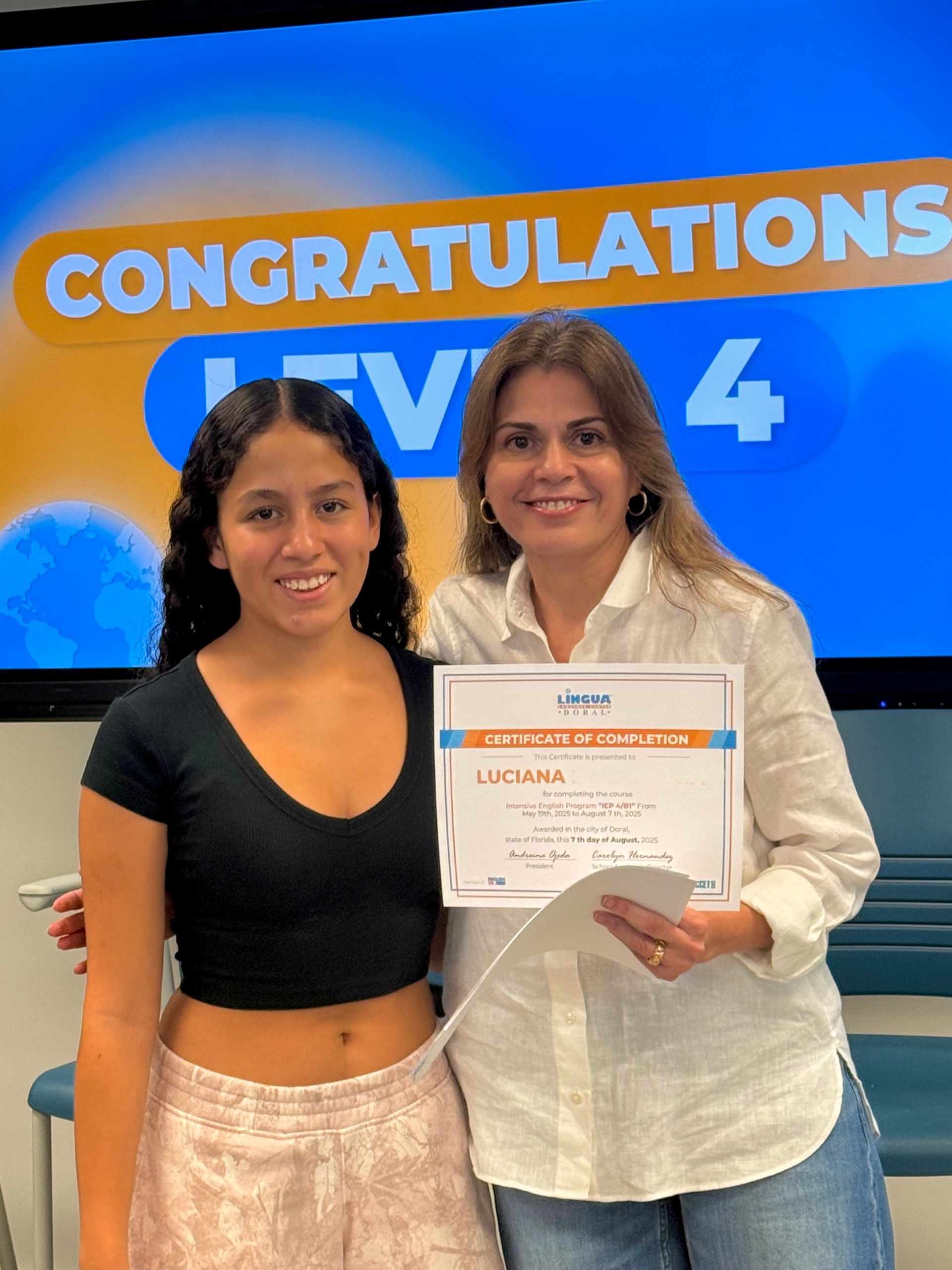 Two women posing with a certificate in front of a “CONGRATULATIONS” and “UFW 4” sign