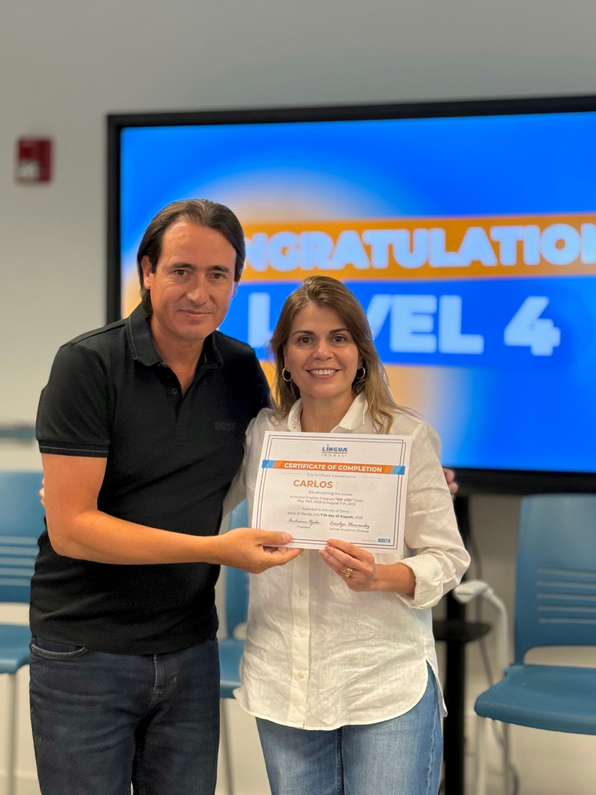Two people holding a certificate in front of a screen that says “Congratulations Level 4”