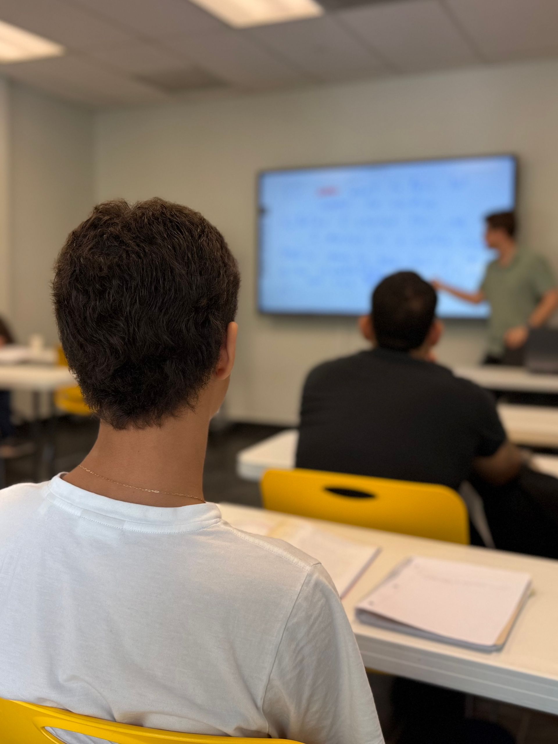 Classroom lecture with students seated facing a presenter near a screen