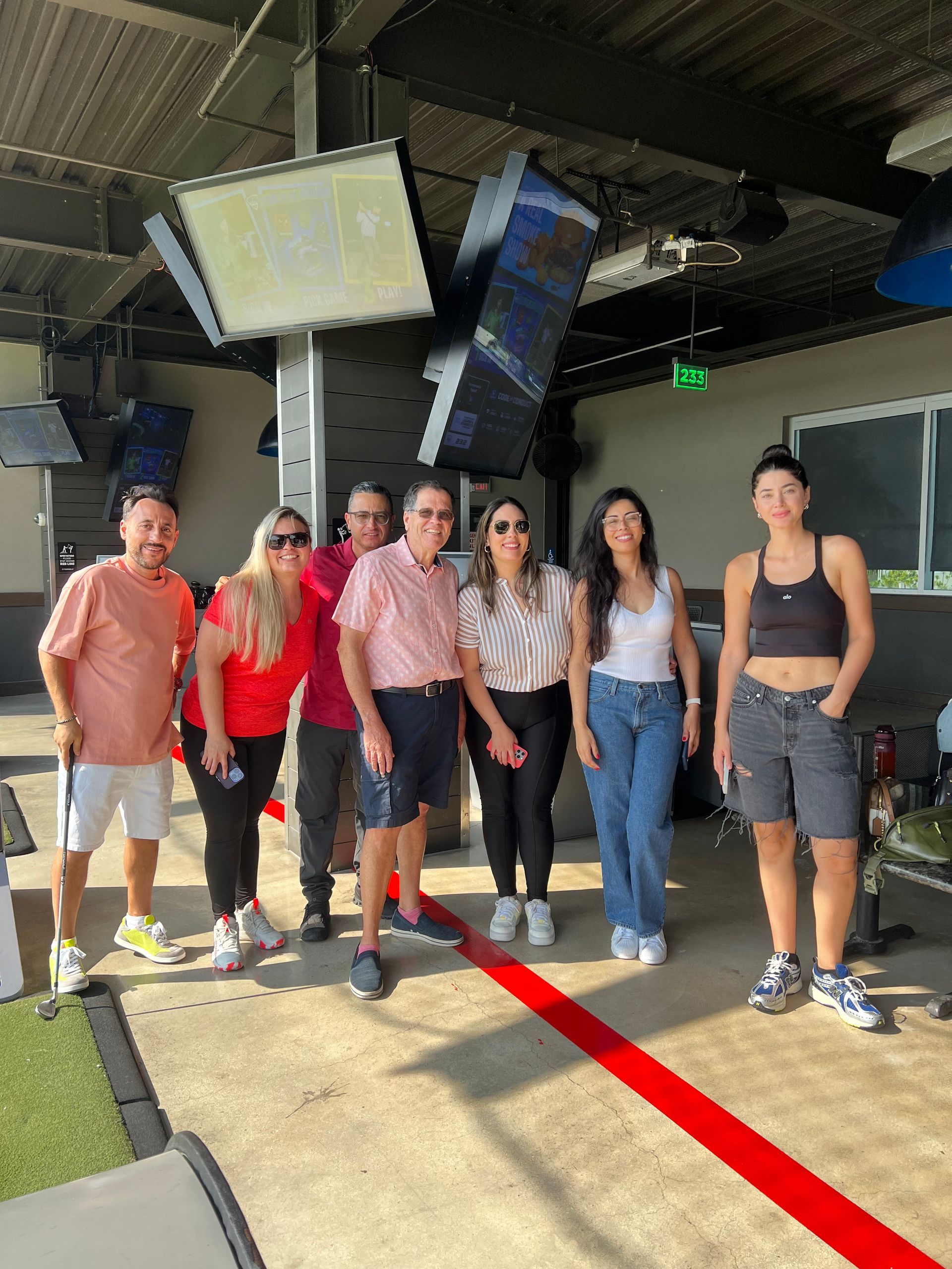 Six people standing together indoors near tennis courts, posing under hanging screens.