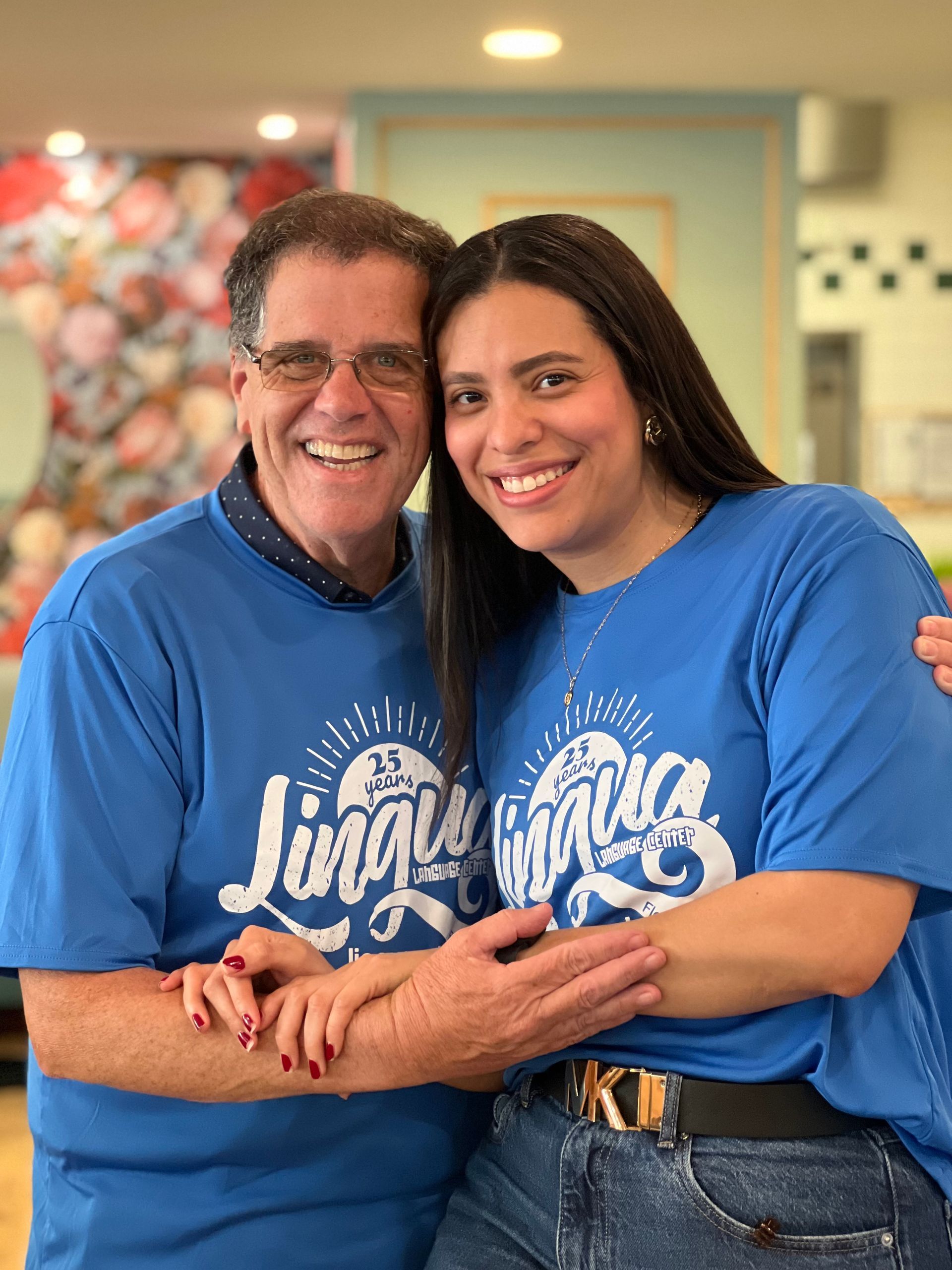 Two people in blue shirts smiling and hugging indoors