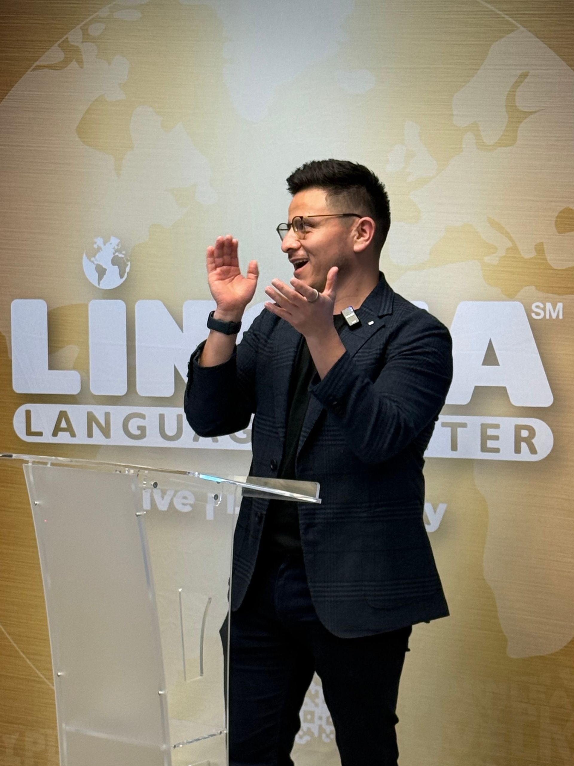 Man speaking and clapping at a podium in front of a “Language Center” wall sign