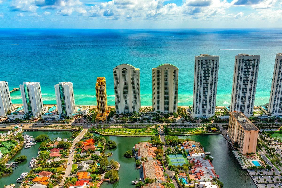 Aerial view of beachfront condos beside turquoise ocean and a landscaped pool area