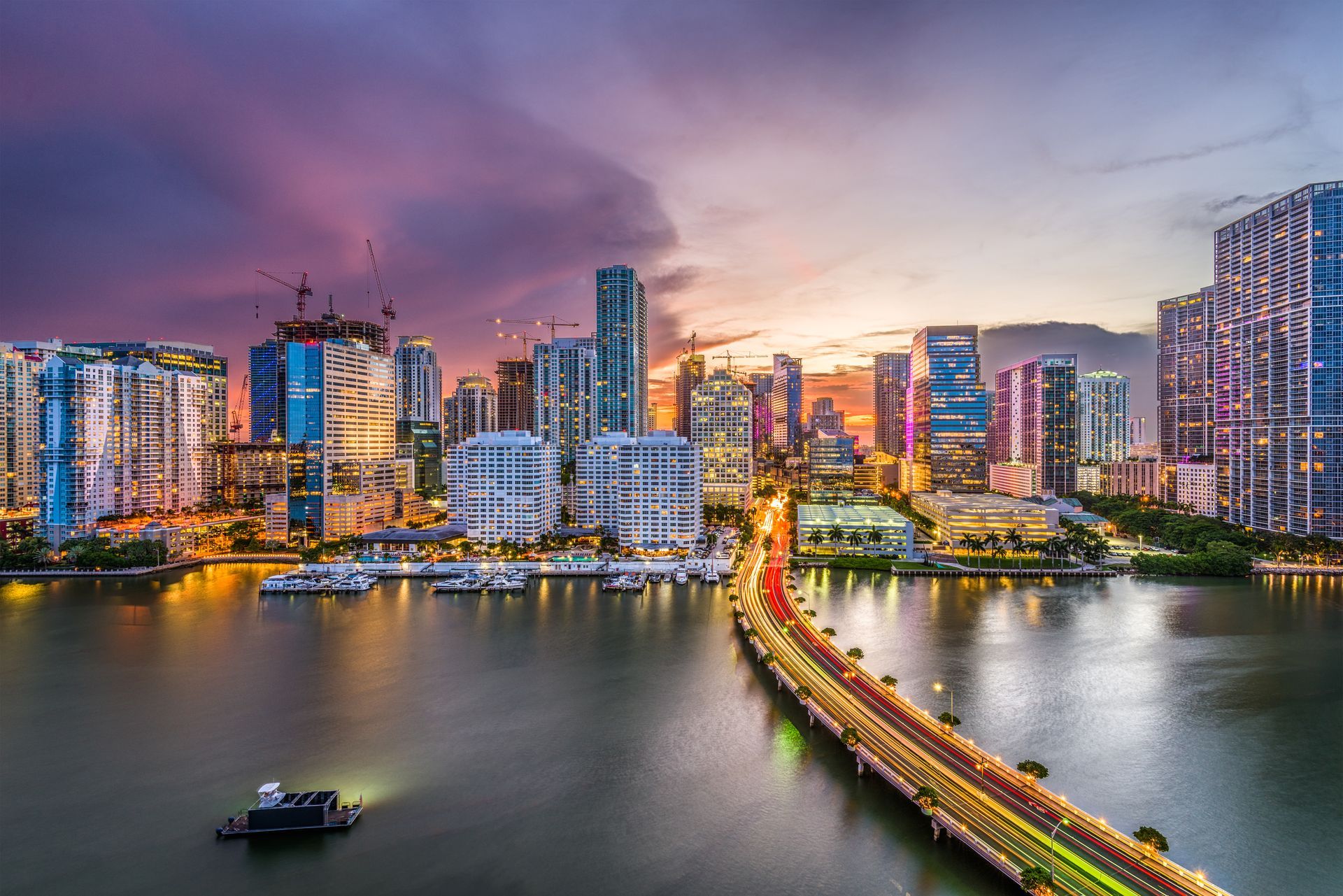 City skyline at dusk with colorful high-rises and a lit bridge over calm water