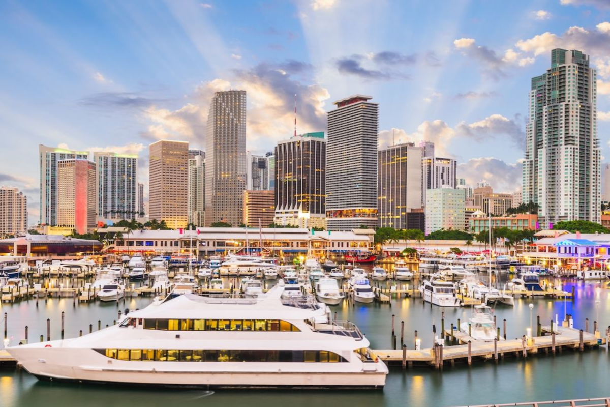 Sunlit marina skyline with yachts, colorful waterfront buildings, and blue sky with clouds