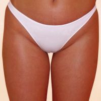 A woman is wearing a white thong and standing with her legs crossed.
