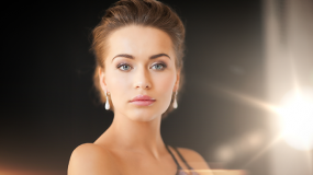 A woman in a black dress and earrings is looking at the camera.