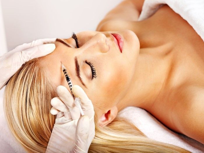 A woman is getting a botox injection in her forehead.
