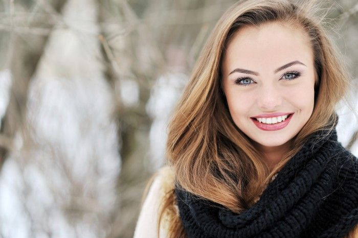 A woman wearing a scarf and a sweater is smiling in the snow.