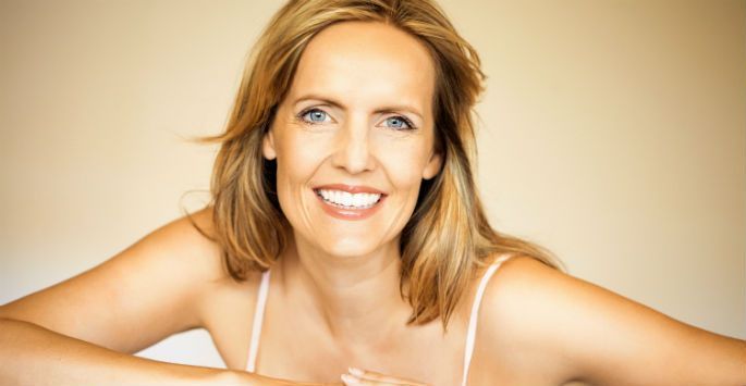 A woman in a white tank top is smiling for the camera.