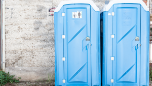 Two blue portable toilets beside a stone wall