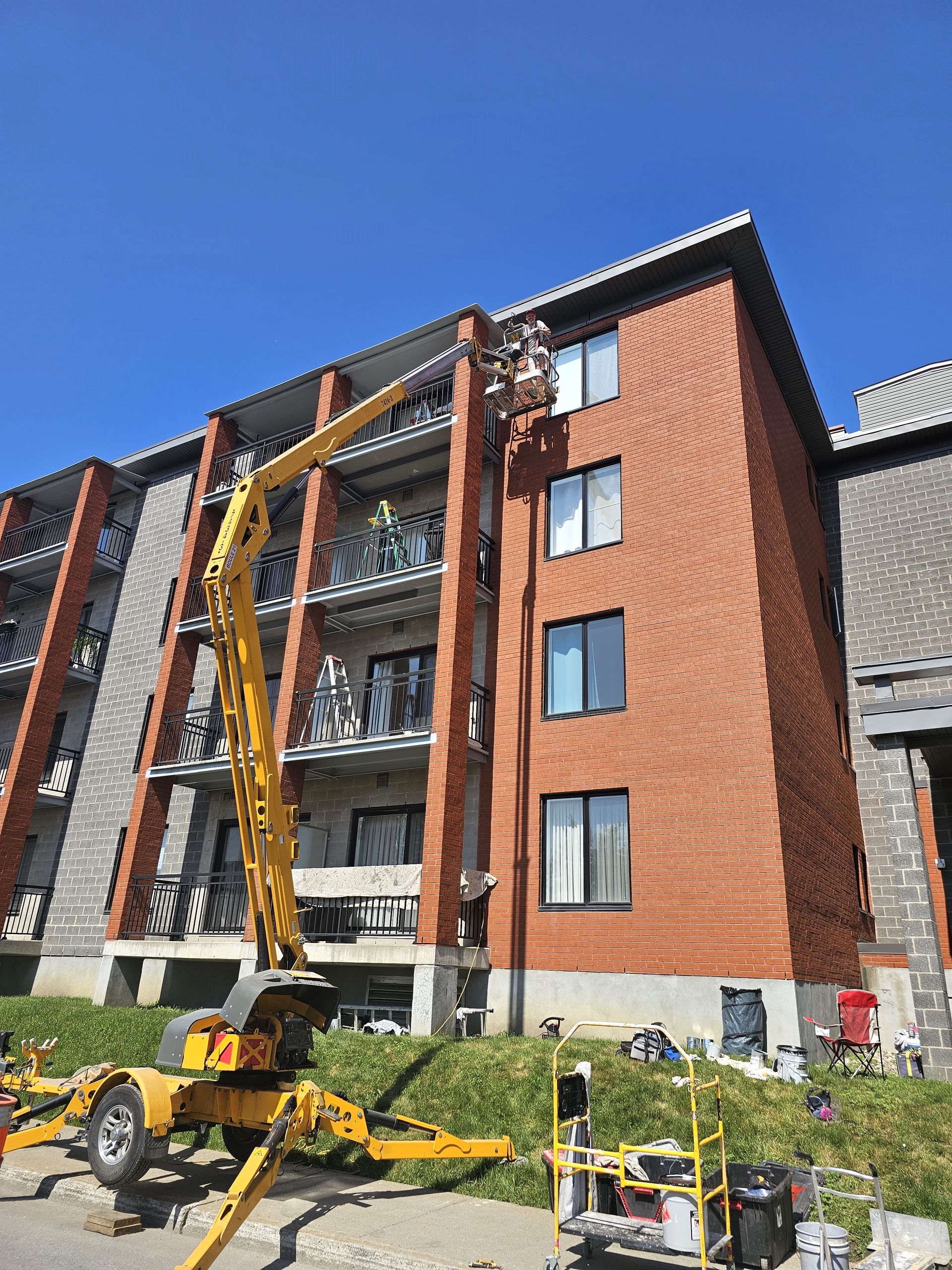 Une grue jaune est assise devant un grand bâtiment en brique.