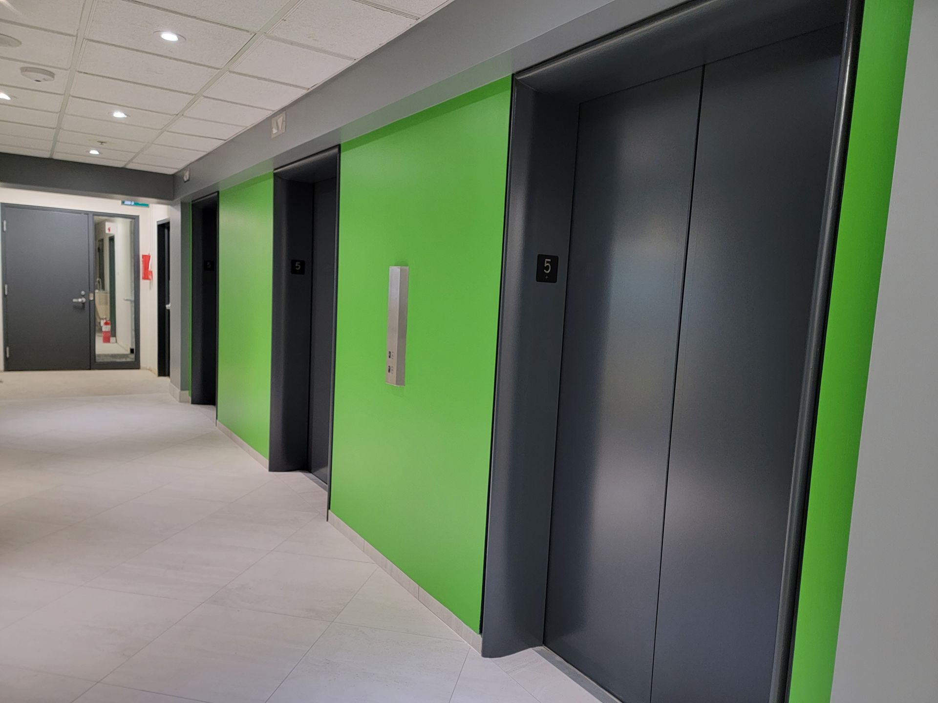 Une rangée d'ascenseurs dans un immeuble aux murs verts.