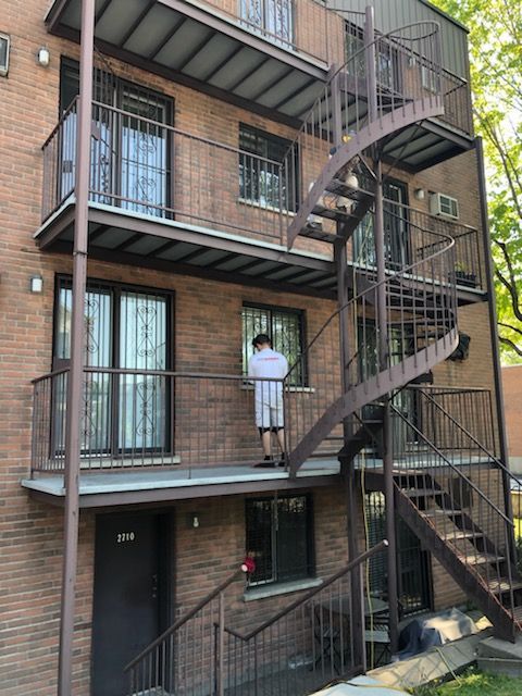 Un homme se tient sur le balcon d’un immeuble avec des escaliers