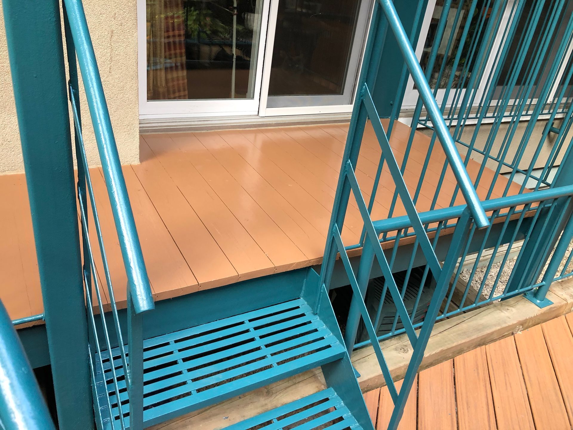 Un escalier en métal bleu menant à une terrasse en bois.