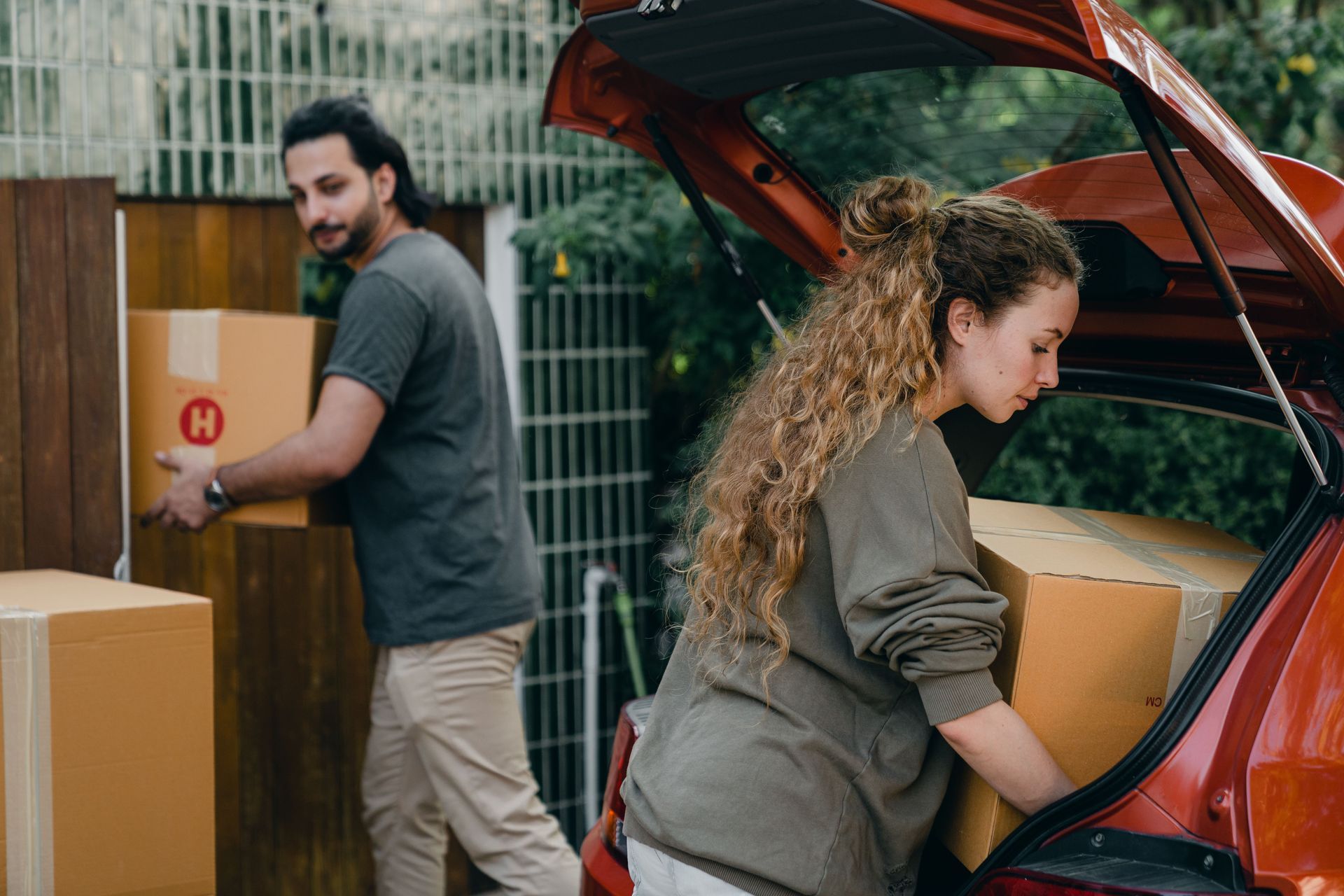 Two people loading boxes into a red car with its trunk open