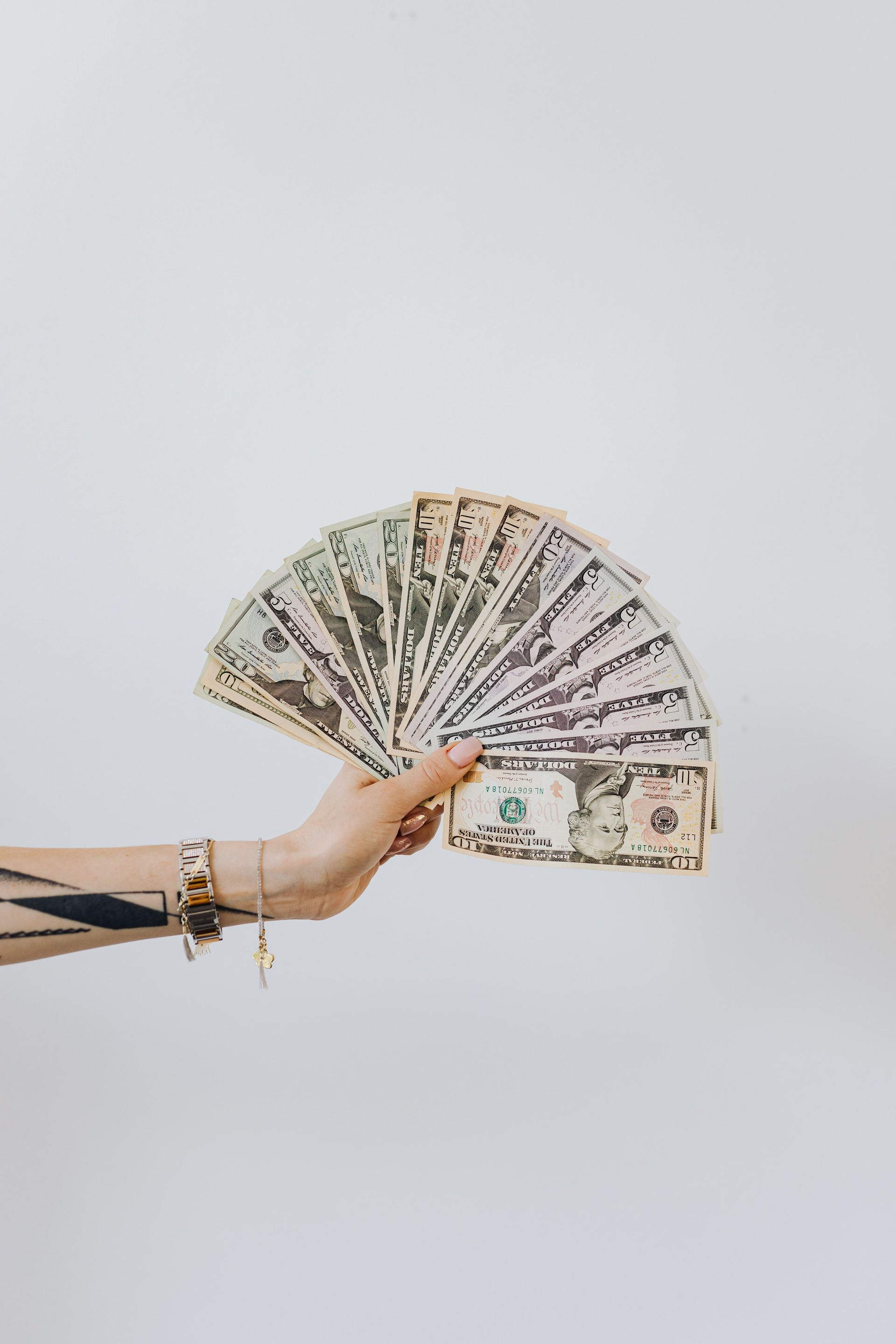 Hand holding a fan of US dollar bills against a plain white background