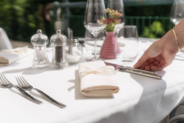 Set dining table with white cloth, glassware, napkins, and a hand placing cutlery at the edge
