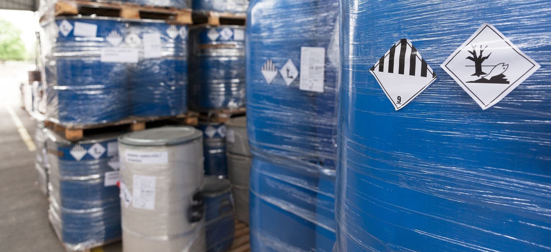Des barils bleus empilés sur des palettes, avec des étiquettes d'avertissement de danger.