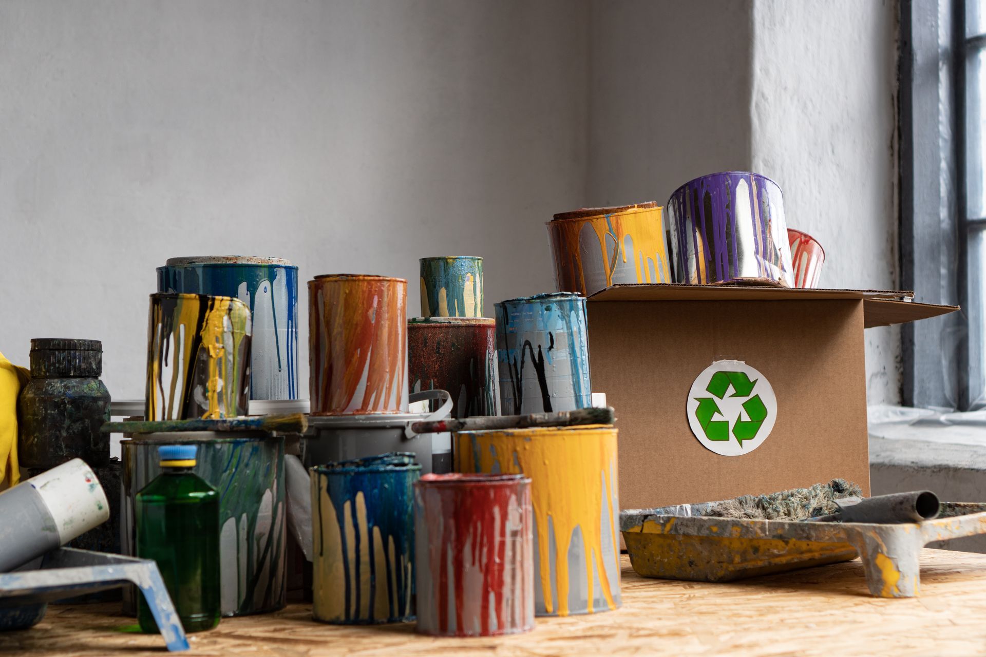 Pots de peinture dégoulinant près d'un conteneur de recyclage, fenêtre en arrière-plan.