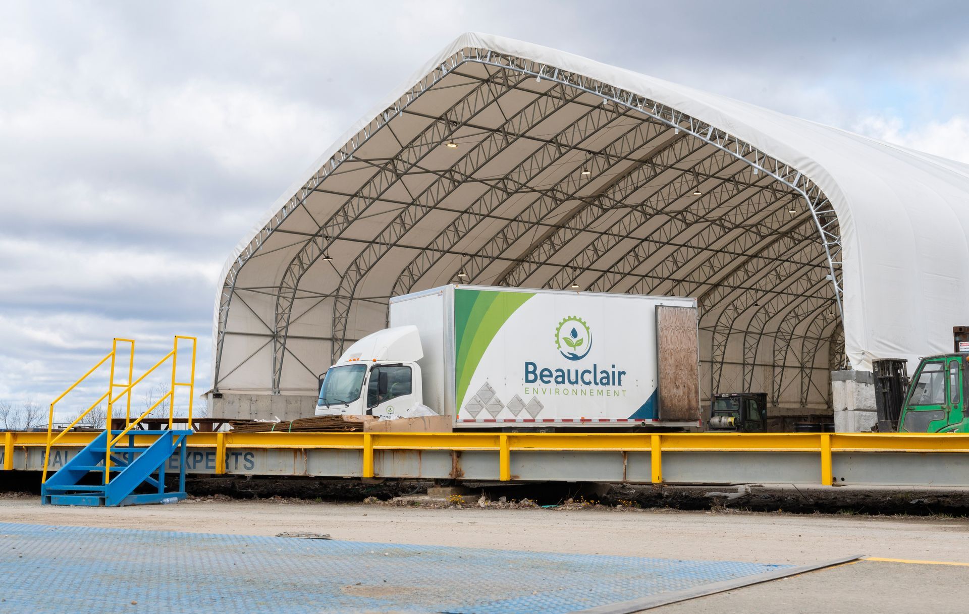 Un camion portant le logo « Beauclair » recule dans un quai de chargement sous une structure blanche en forme de tente.