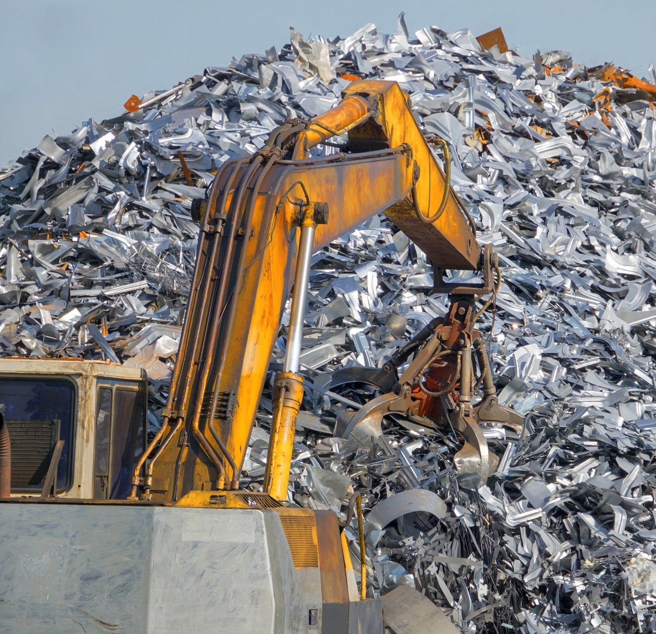 Bras d'excavatrice soulevant de la ferraille d'un grand tas dans une cour de recyclage.