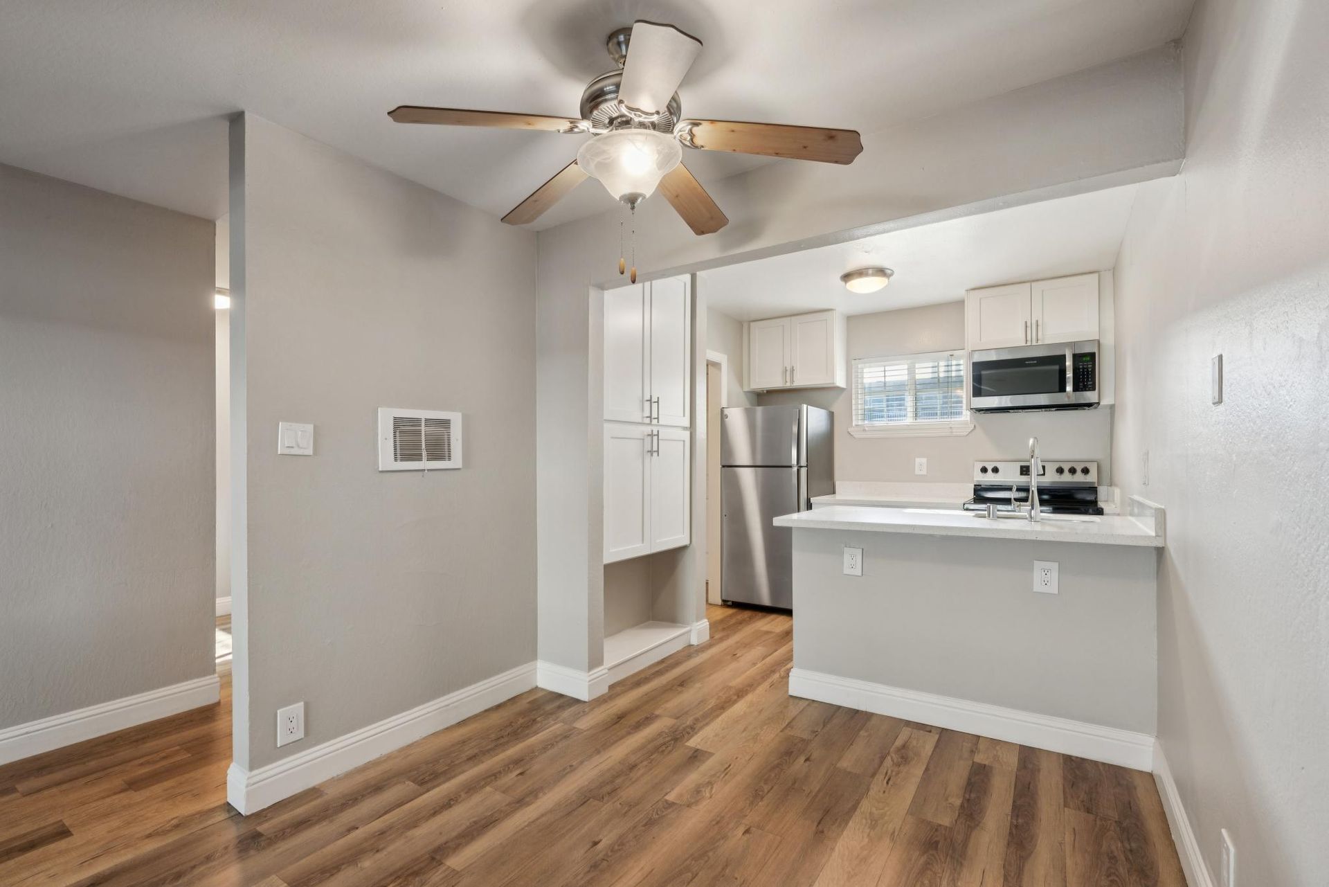Interior of a kitchen and dining area with hardwood floors, white cabinets, and stainless steel appliances.