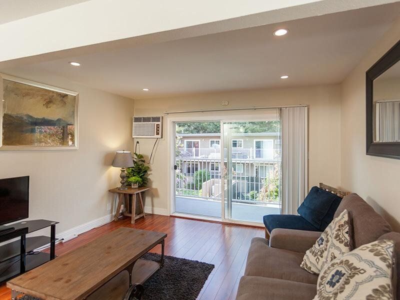 Living room in an apartment with sofa, coffee table, TV, and sliding glass balcony door.