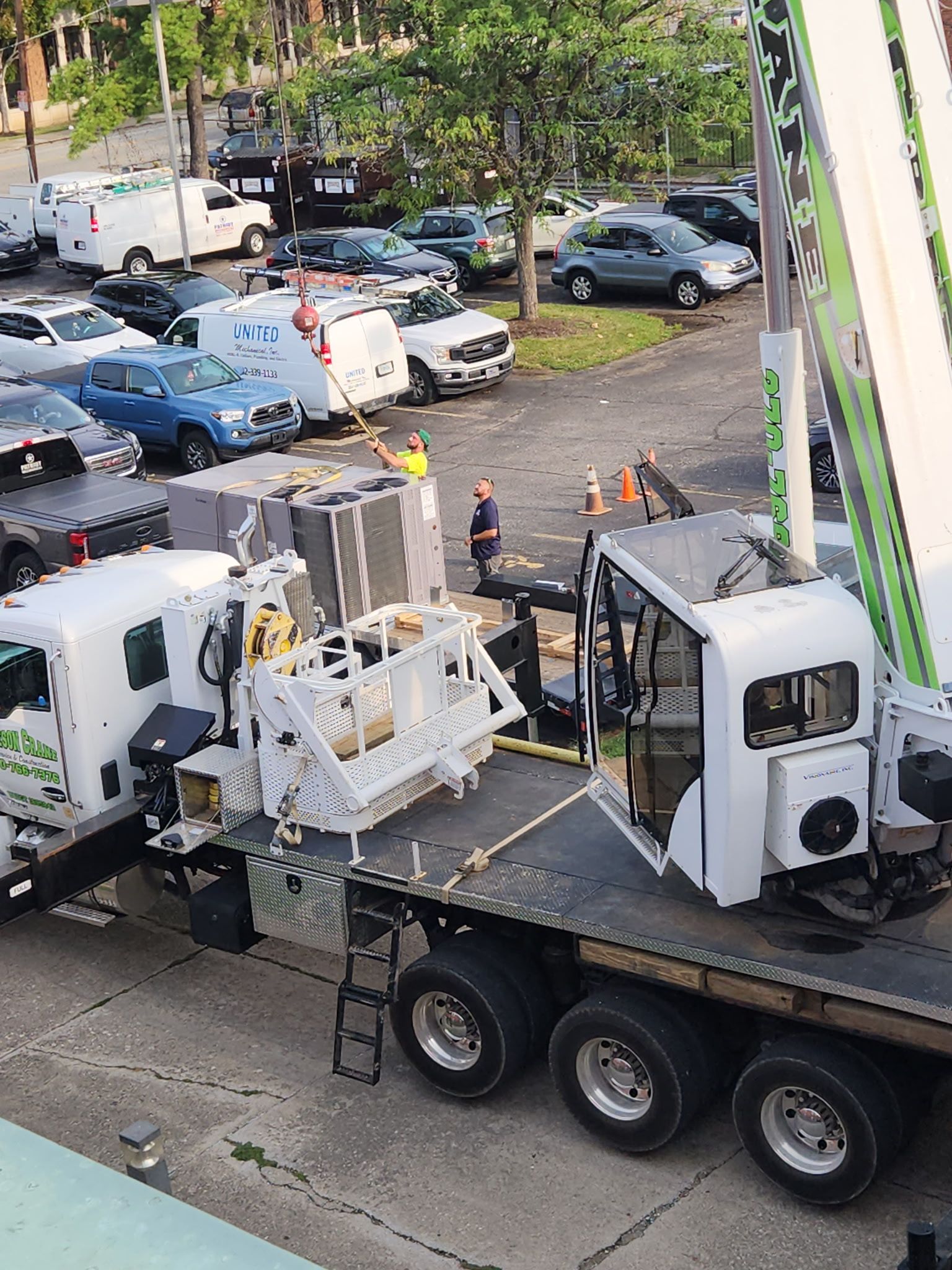 White utility truck with lift equipment in a parking lot, viewed from above, with cars and trees nearby
