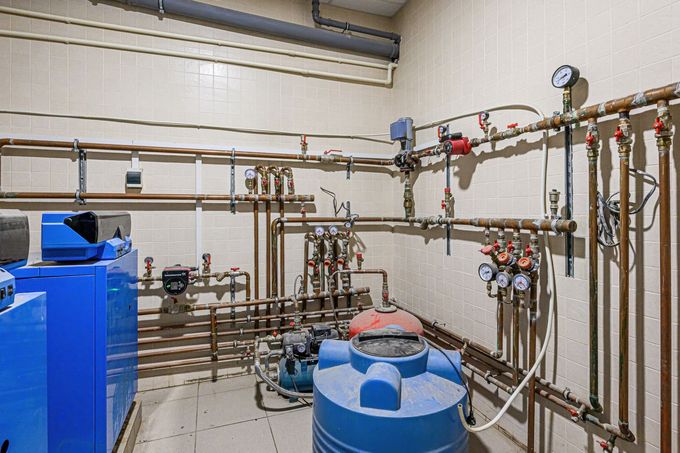 Mechanical room with blue tanks, copper pipes, gauges, and valves along the wall