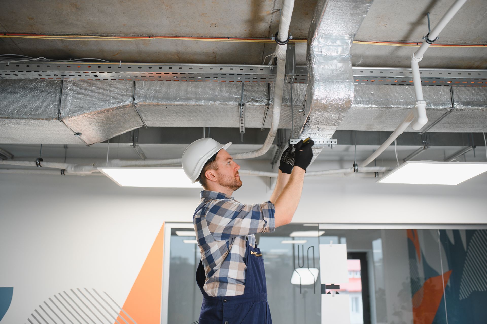 Worker in hard hat inspecting ceiling pipes in an unfinished room