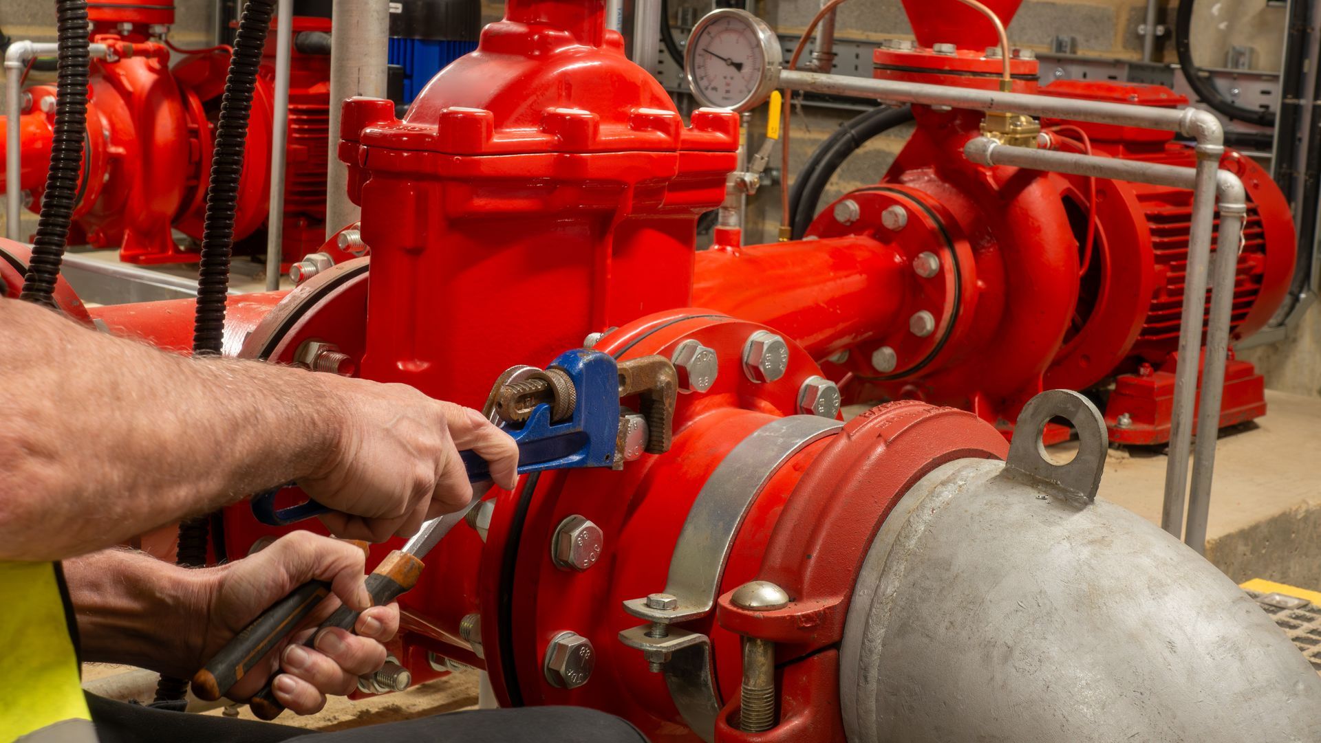 Worker adjusting a valve on bright red industrial piping in a mechanical room