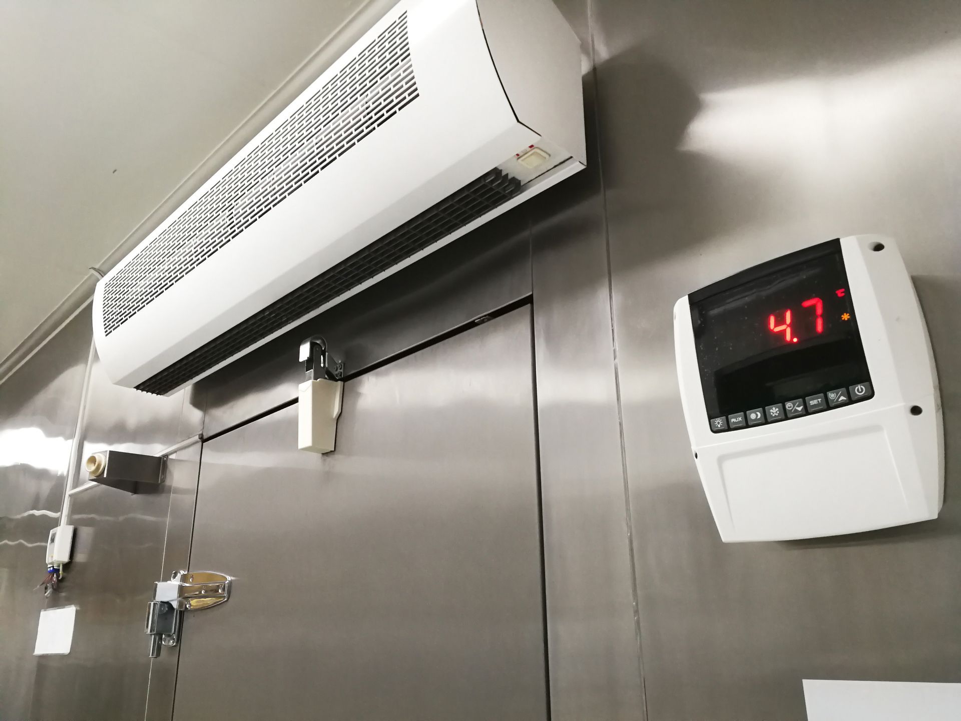 Commercial kitchen wall with stainless-steel equipment, overhead vent, and a digital temperature display reading 47°F Commercial kitchen wall with stainless-steel equipment, overhead vent, and a digital temperature display reading 47°F