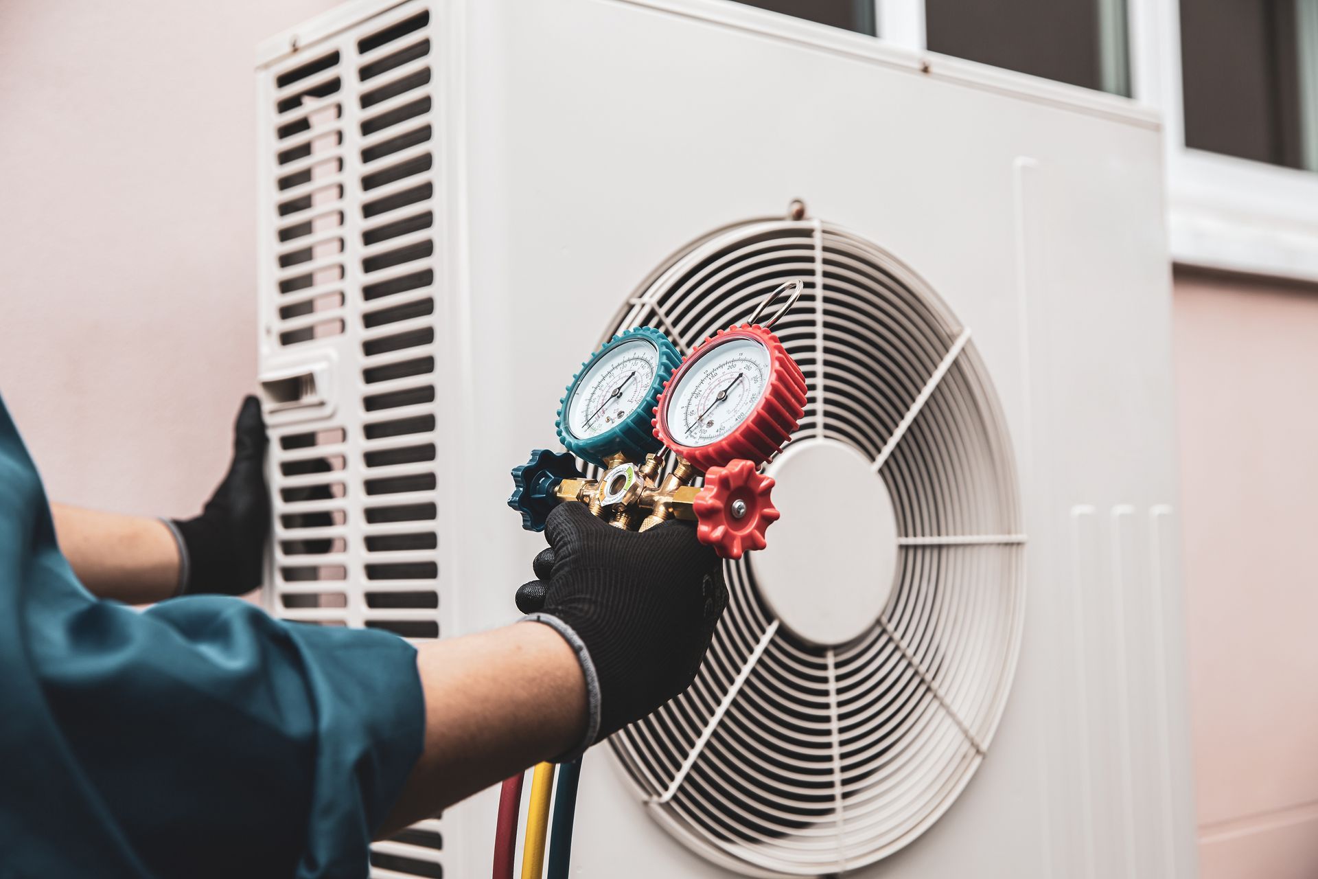 Technician checking HVAC unit gauges beside an outdoor air conditioner fan