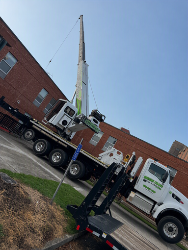Tow truck lifting a white truck in front of a red brick building on a sunny day