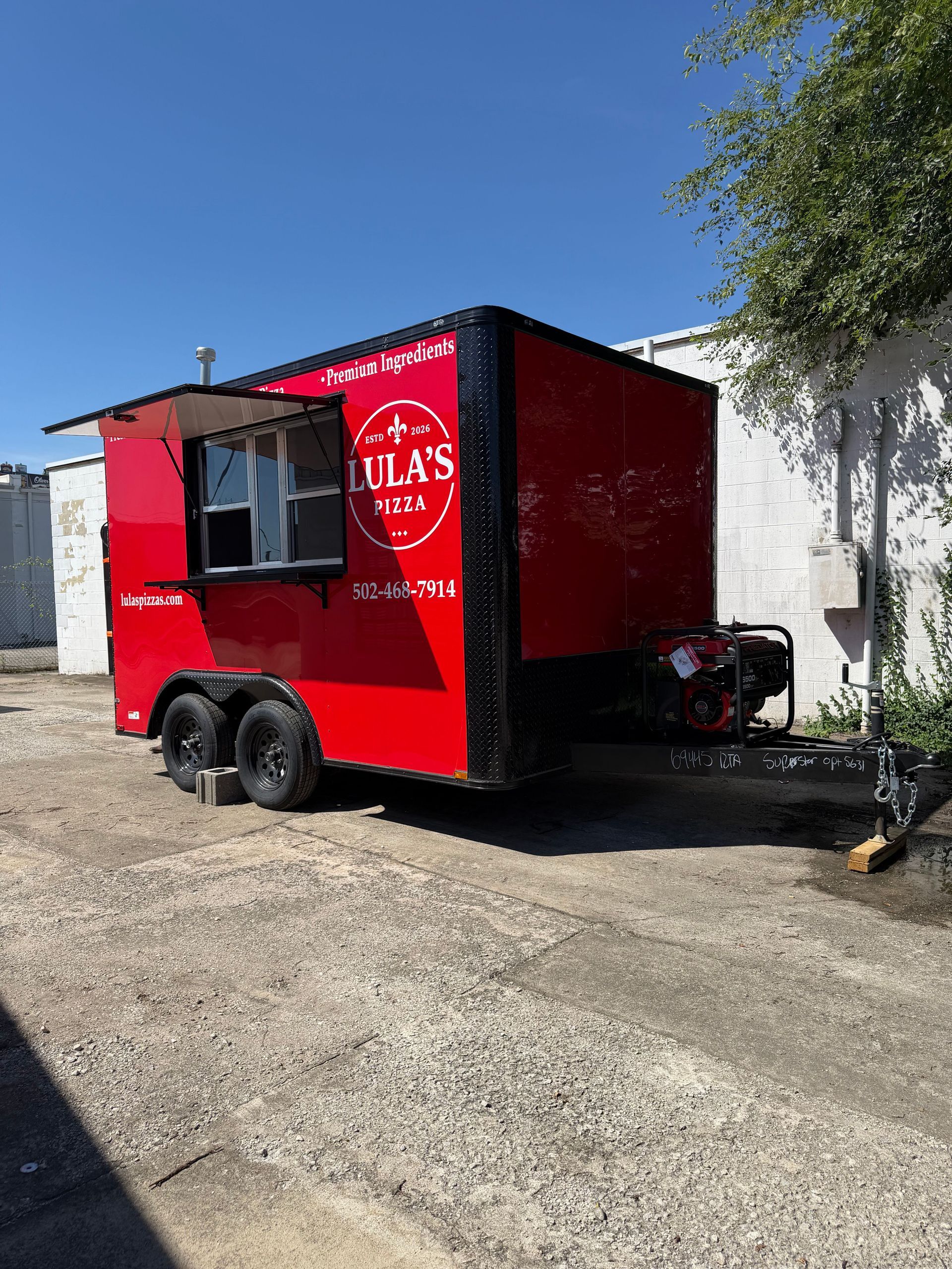Red food trailer with serving window parked on gravel under a blue sky