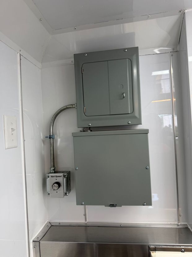 Gray electrical panels mounted on a white utility room wall above a metal counter