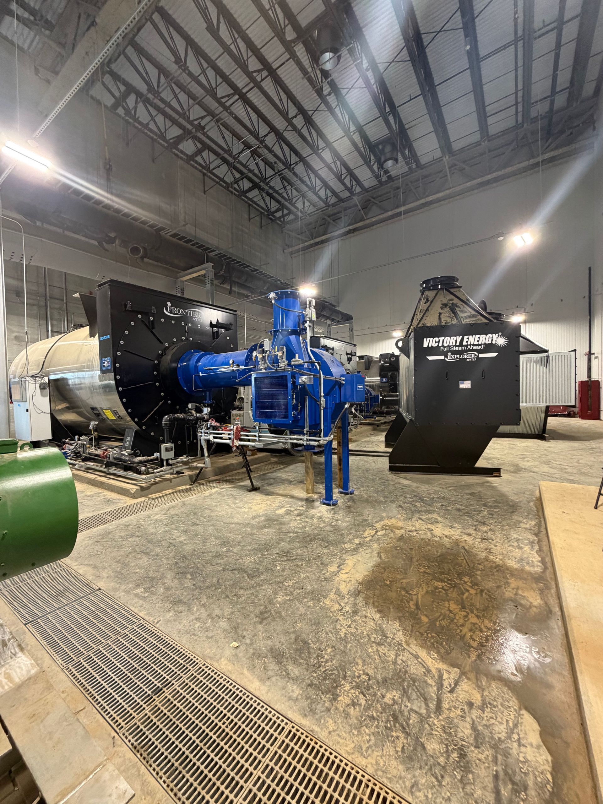 Blue industrial machinery inside a large warehouse with concrete floor and high metal ceiling