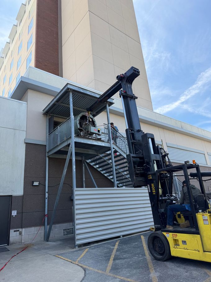 Forklift lifting workers on an outdoor metal stairway beside a tall building