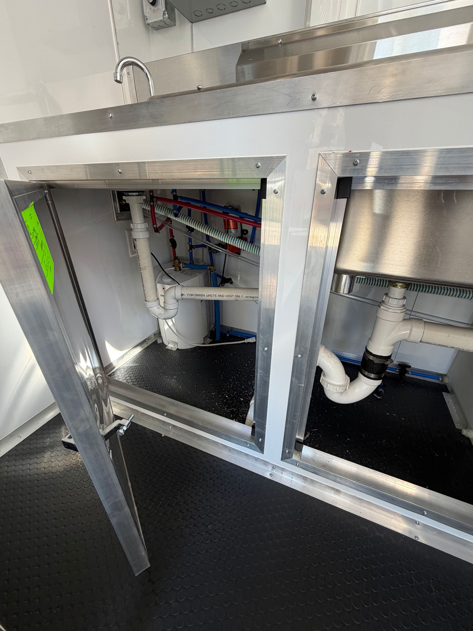 Open cabinet under a sink with exposed plumbing, pipes, and wiring in a utility room Open cabinet under a sink with exposed plumbing, pipes, and wiring in a utility room