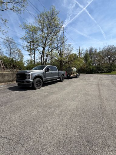 Black pickup truck and small trailer parked on a gravel lot under a blue sky with trees in the background