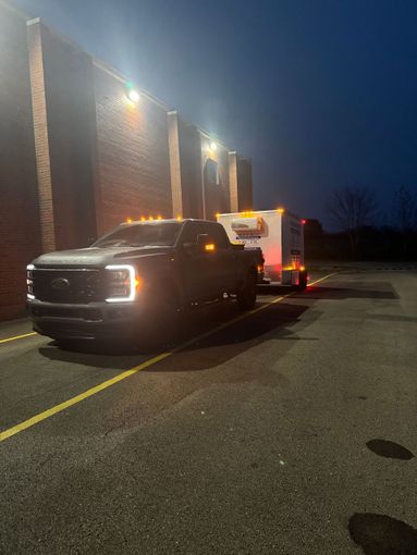 Tow truck parked beside a brick building at night, lights glowing on a wet parking lot.