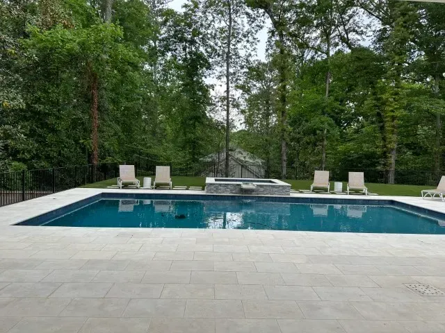 Swimming pool with lounge chairs, surrounded by trees.