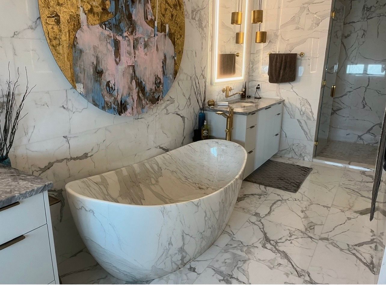 Luxurious bathroom with marble walls and a standalone tub, gold accents, and artwork.