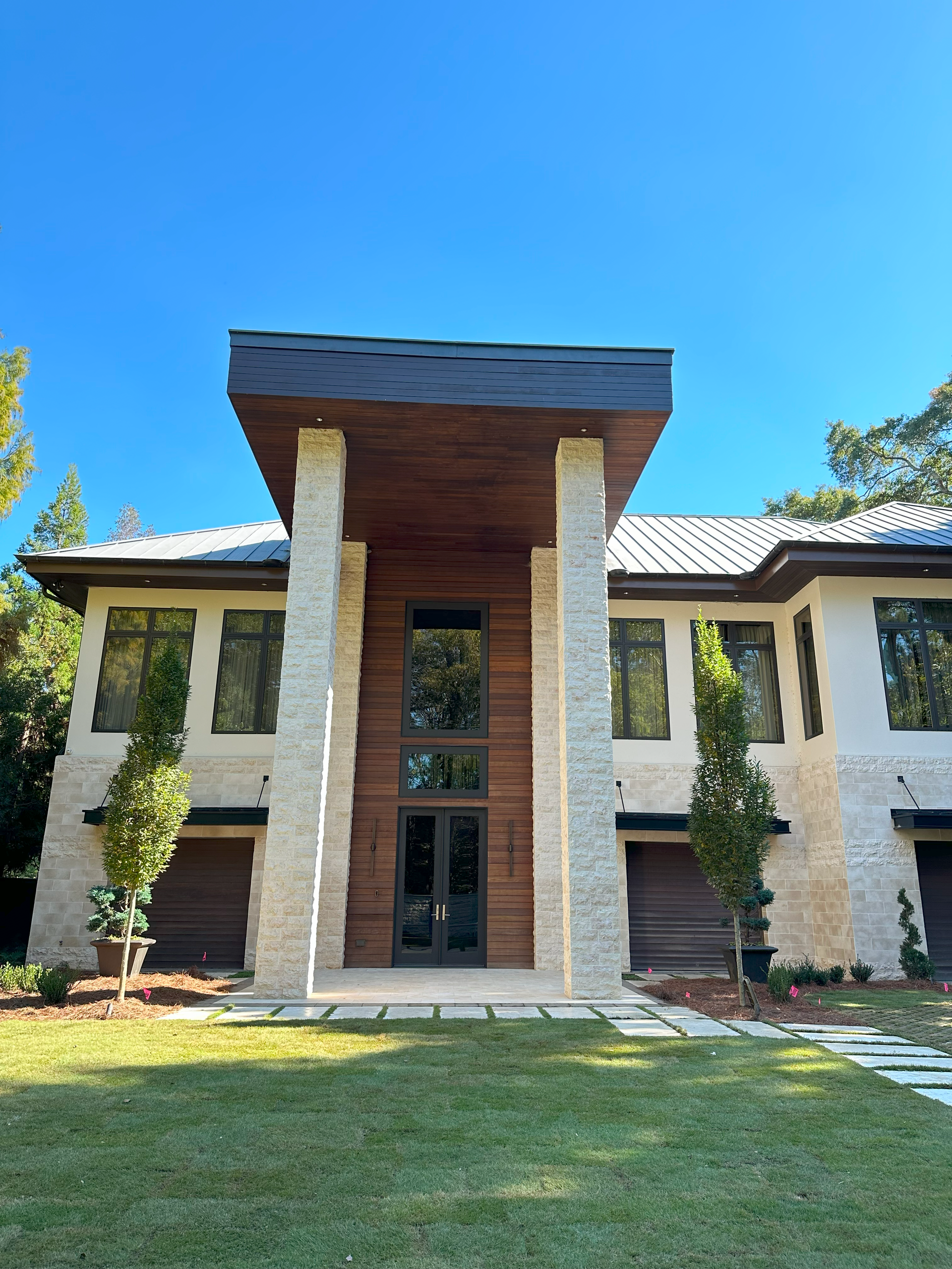 Modern house with stone columns and wooden accents, blue sky.