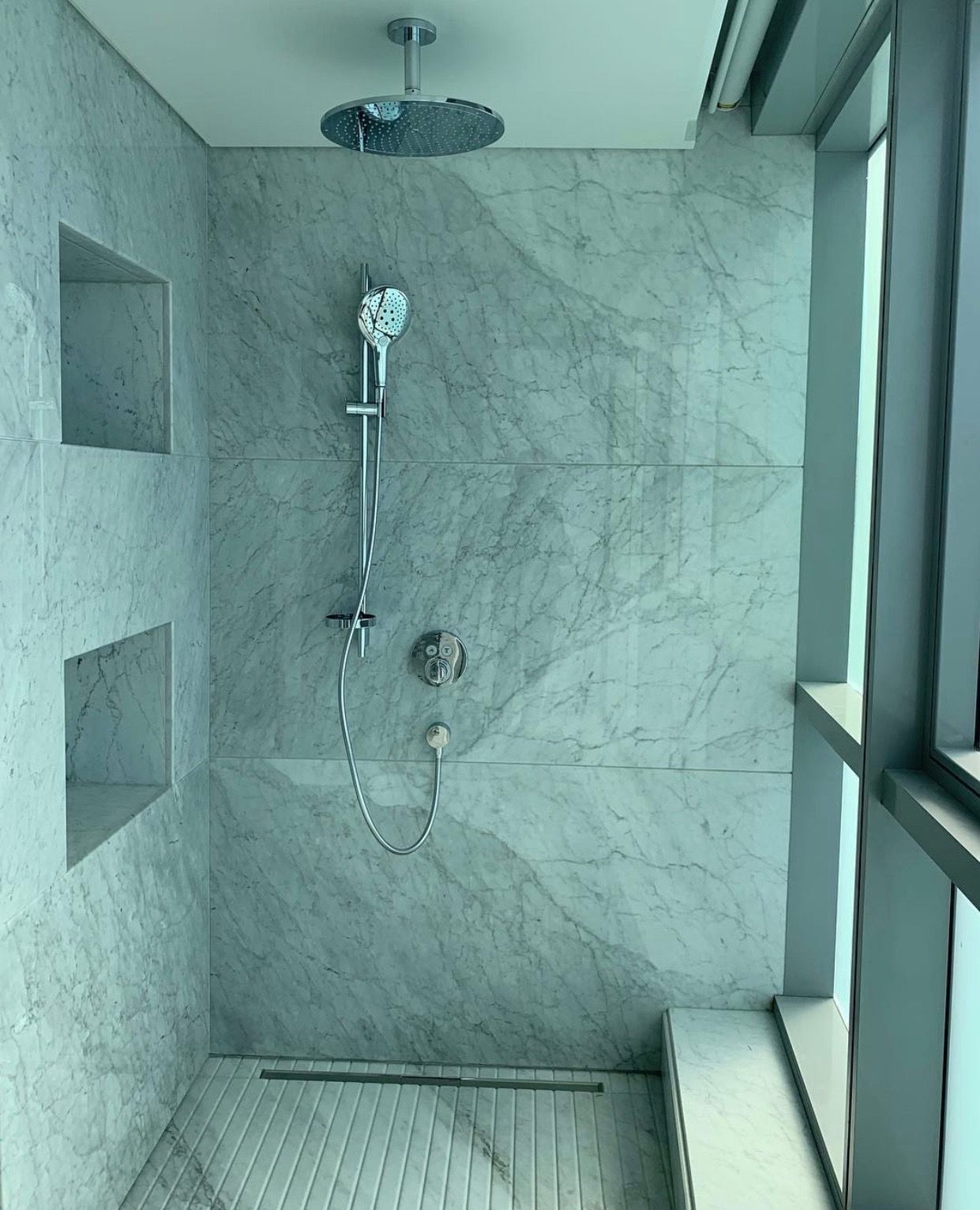Modern shower with marble-like tiled walls, recessed shelves, and rain showerhead.